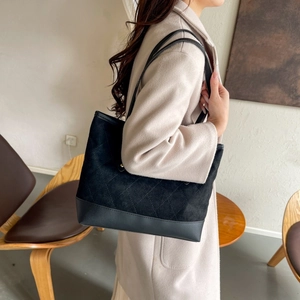 Détail du sac cabas noir matelassé avec textures cuir porté sur un manteau en laine