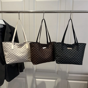 Minimalist tote bag with M-letter print in white, caramel, and black shown on a door