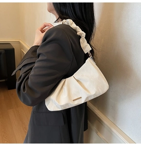 Close-up of pleated beige cloud shoulder bag with golden hardware and ruffled strap