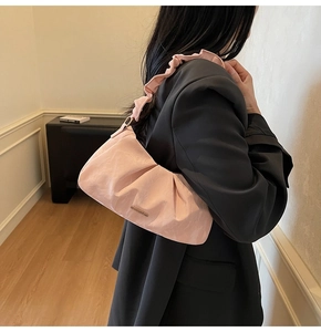 Close-up of pink pleated shoulder bag featuring glossy texture and metal logo plate