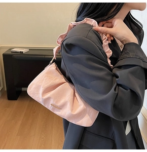 Detail of pink pleated cloud bag featuring ruffled strap and golden metal logo bar