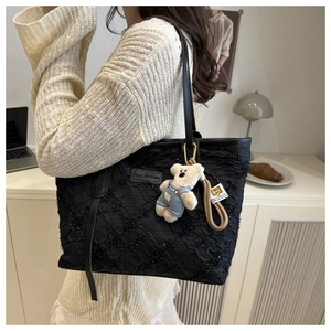 Detail of black quilted tote bag with shimmer finish and cute bear charm pendant