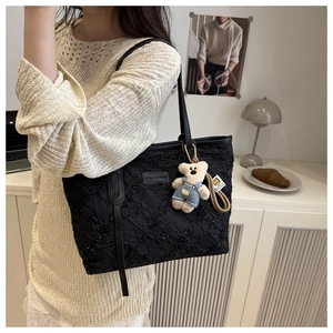 Detail of black pleated tote bag with glitter texture and cute plush bear charm