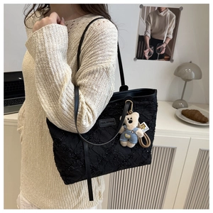 Detail of black woven tote bag with sparkling texture and blue overalls bear charm