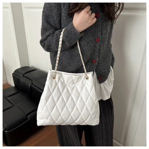 Close-up of a white quilted tote bag with gold-tone chain straps on a female model