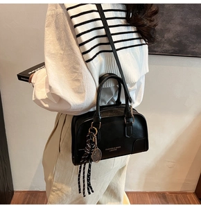 Close-up of black leather bag featuring gold lettering, tennis racket charm and silk ribbon