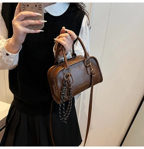 Brown Boston style handbag with striped charm and gold text on a polished surface
