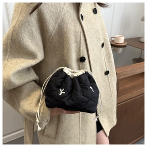 Detail of black quilted drawstring pouch with white embroidery held by a model