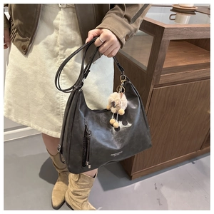Detail of black faux leather hobo bag featuring white text logo and brown pompom charm