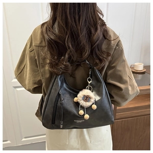 Close-up of black leather hobo bag with teddy bear charm worn by a model