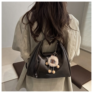 Detail of dark brown leather tote bag featuring a cute plush bear charm on the strap