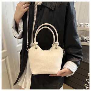 Detail view of cream bucket bag with gold hardware and logo on a leather jacket model