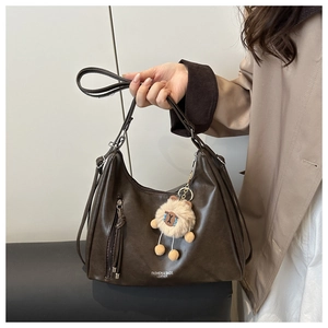 Detail of vintage brown leather bag with tassel and plush charm on a beige trench coat