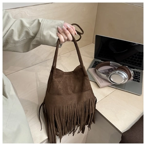 Détail du sac à main en daim marron à franges avec doubles anses sur un bureau