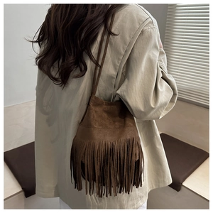 Vue détaillée du sac seau en daim marron foncé avec franges porté par un mannequin