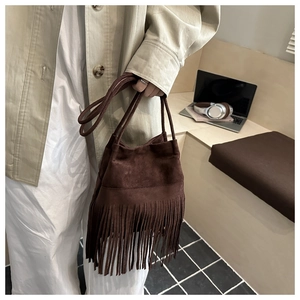 Détail du sac seau en daim marron foncé à franges longues dans un décor de bureau moderne