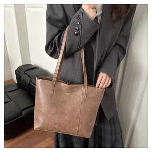 Détail d'un sac cabas marron vintage avec lettrage doré et bandoulière en cuir souple