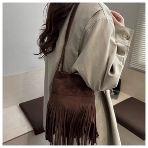 Détail d'un sac bandoulière en daim marron foncé avec de longues franges sur un trench