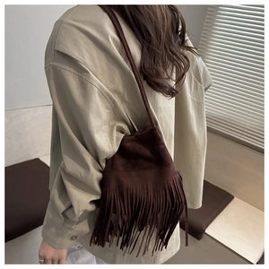 Détail du sac seau en daim marron foncé avec de longues franges sur une chemise beige