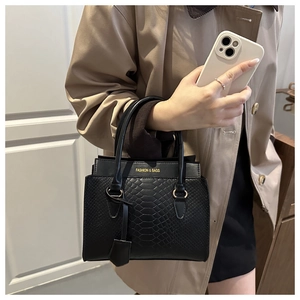 Detail einer schwarzen Handtasche mit Krokostruktur und Goldschrift, von Model getragen