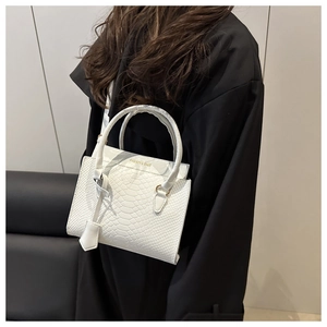 Detail der weißen Handtasche mit Krokodilprägung, Goldschrift und Rundgriffen