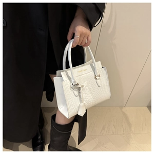 Detail einer weißen Handtasche mit Krokodilprägung und goldenem Fashion-Schriftzug