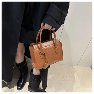 Detail einer dunkelbraunen Handtasche mit Krokodilmuster getragen von einem Model