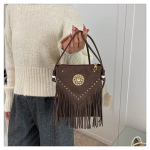 Close-up of bohemian brown suede bag with gold rivets, fringe, and ornate emblem detail