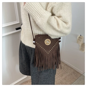 Detail of bohemian brown suede bucket bag with gold rivets, tassels, and vintage medal