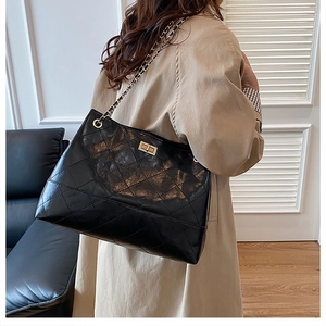 Close-up of black quilted tote bag with gold chain strap worn over a khaki trench coat