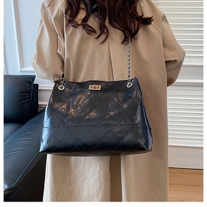 Close-up of black quilted tote bag with golden turn-lock closure and chain strap