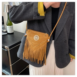 Detail of mustard yellow suede tassel bucket bag with gold rivets and bohemian metal ornament
