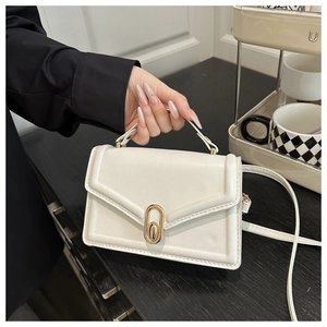 Detailed close-up of a white square handbag with golden oval twist lock and top handle