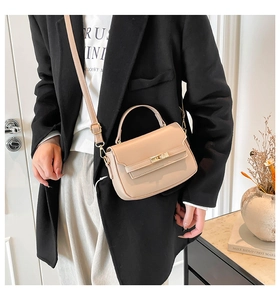Detail of beige saddle bag with gold swivel lock and adjustable strap on a model