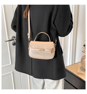 Close-up of beige leather mini handbag with gold twist lock on a black coat background