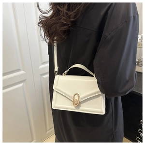 Close-up of white leather handbag with golden oval twist-lock worn by a model