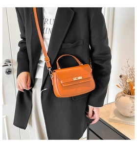 Detail of an orange leather crossbody bag with gold twist lock on a minimalist blazer outfit