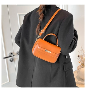 Detail of vibrant orange satchel with gold metallic buckle on a black blazer background