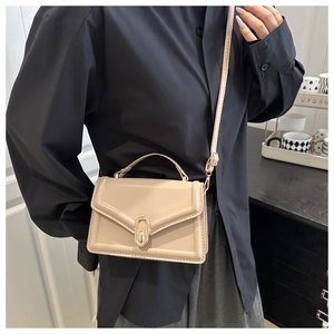 Detailed view of beige box-shaped crossbody bag with gold metal buckle on black background