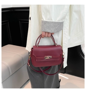 Detail of burgundy leather handbag with metal turn-lock and adjustable shoulder strap