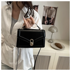 Detail of a black leather crossbody bag with a gold oval lock on a minimalist background