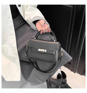 Detail of a structured black leather handbag with gold metal clasp and top handle