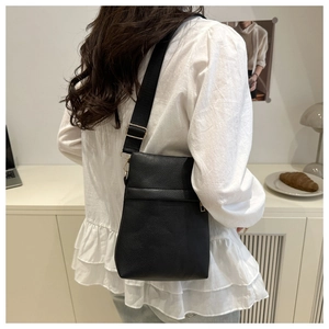 Close-up of black PU leather crossbody bag with wide strap and golden hardware on a model