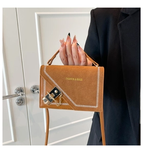 Detail of brown suede crossbody bag featuring white contrast stitching and a gold clasp
