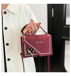 Close-up of burgundy square bag with suede texture, hardware buckle, and white stitching