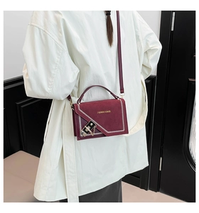 Detail of burgundy matte shoulder bag with white stitching and decorative gold chain