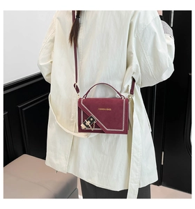 Detail of burgundy crossbody bag featuring white zigzag stitching and gold lock closure