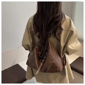 Detailed view of large dark brown leather backpack styled with a beige trench coat