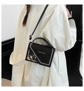 Detail of black crossbody bag with white stitching and gold hardware on white trench coat