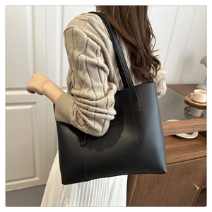 Minimalist black leather tote bag with long straps worn on shoulder with casual outfit